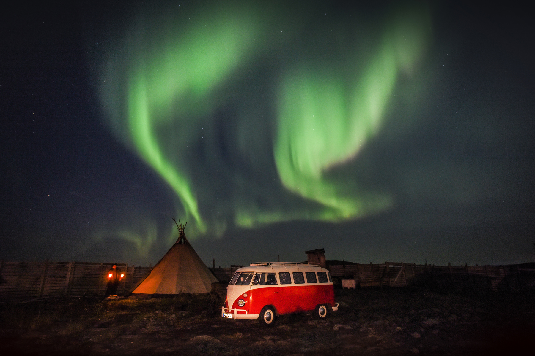 Roter VW-Bulli neben einem Tipi unter grünen Nordlichtern