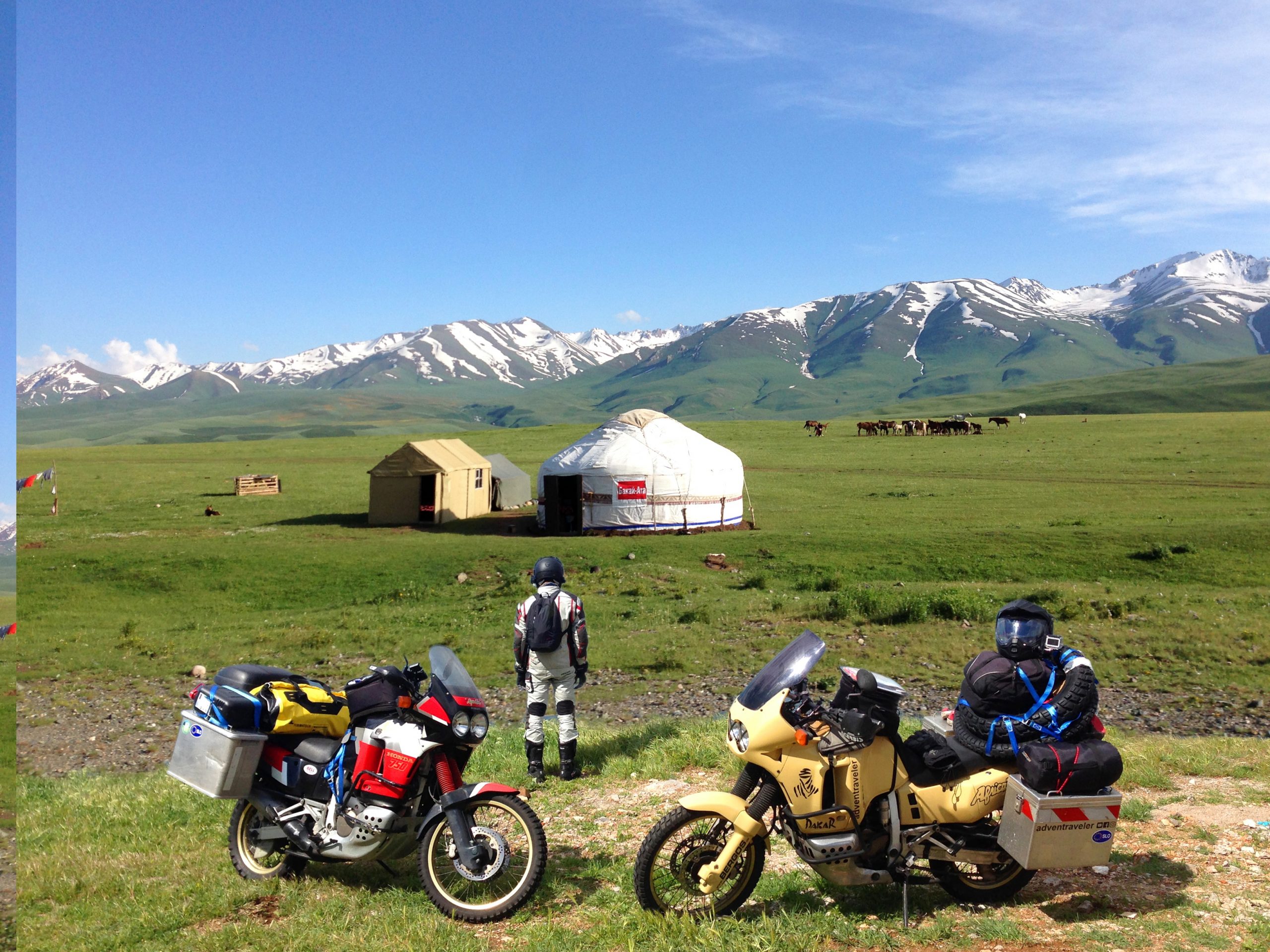 Zwei Reisemotorräder vor Jurten und schneebedeckten Bergen auf dem Landweg in die Mongolei
